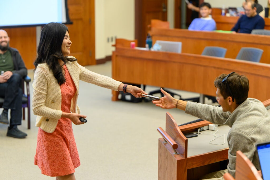 Kelly Lee (left) hands remote to person sitting in a caseroom in the Hariri Building at Georgetown McDonough