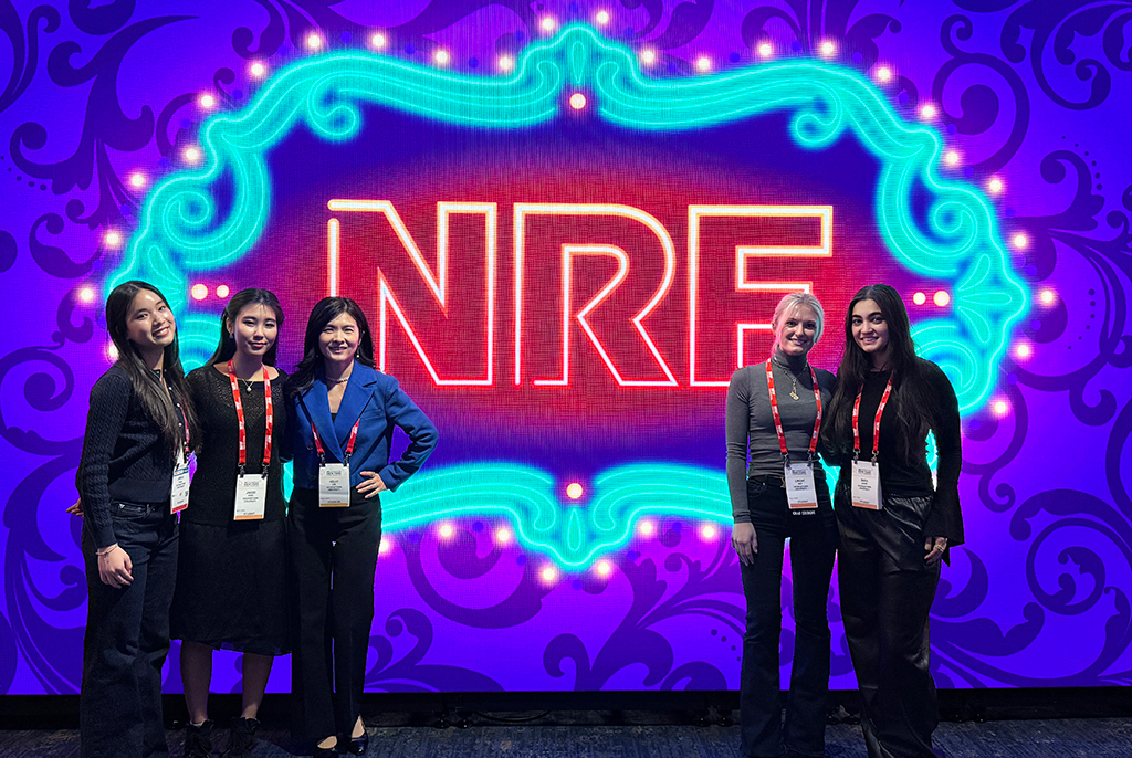 Students and faculty director pose for a photo in front of a neon background that reads NRF, at the NRF Foundation Student Program in New York