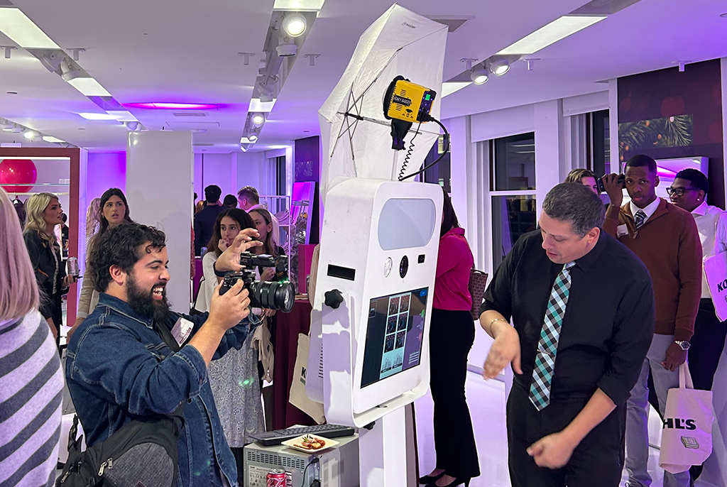 A man takes a photo of a white robot, while another stands next to it, surrounded by other people in the background
